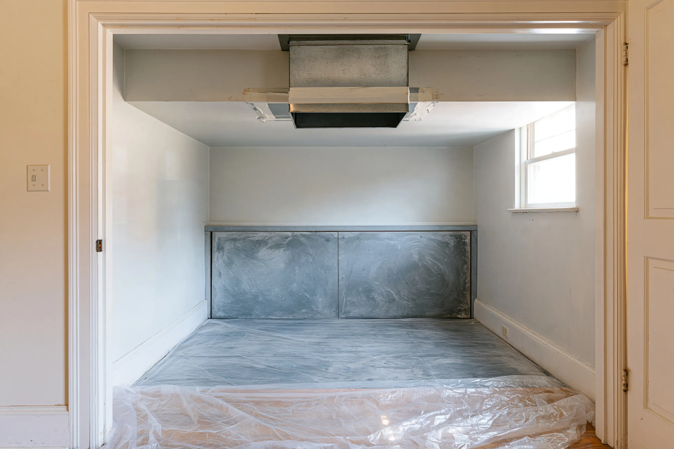 Hall closet with the furnace removed, a metal duct taped over at the opening, a gray panel on the back wall and plastic on the floor